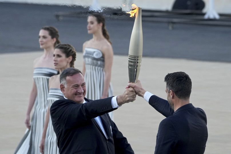 Tony Estanguet, President of Paris 2024, right, receives the Olympic flame from Spyros Capralos, head of Greece's Olympic Committee, in Athens, Friday, April 26, 2024.