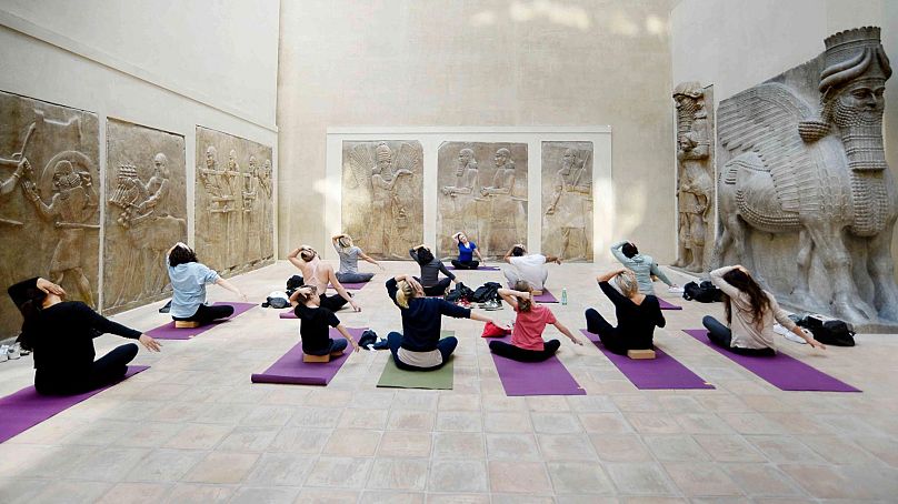 A group exercising on yoga mats in the Louvre's Khorsabad courtyard