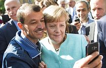 Almanya Başbakanı Angela Merkel, Berlin'e gelen mülteciler için bir tesiste bir mülteci ile selfie çekmek için poz veriyor. 9 Eylül 2015
