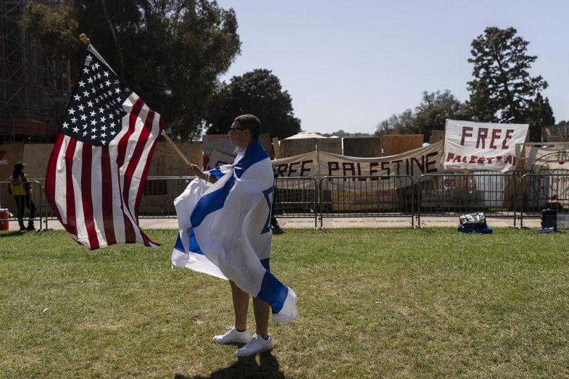 Enrolado numa bandeira israelita, um apoiante pró-Israel caminha com uma bandeira americana perto do acampamento pró-palestiniano no campus da UCLA em Los Angeles