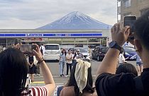 Visitors take a photo in front of a convenient store at Fujikawaguchiko town, Japan, with a backdrop of Mount Fuji 