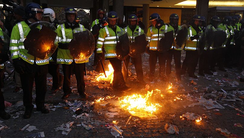Police put out fires started by protesters outside the entrance to Millbank Tower, housing the headquarters of the Conservative Party, during a protest in London