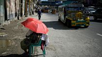 A street vendor uses an umbrella to protect her from the sun along a street in Manila, Philippines. 