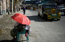 A street vendor uses an umbrella to protect her from the sun along a street in Manila, Philippines. 