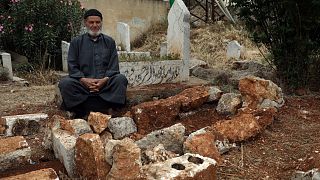 محمد حسن مسطو يجلس بجوار قبر شقيقه لطفي في 7 مايو 2023، في قرية قرقانيا، وهي منطقة ريفية شمال محافظة إدلب، سوريا