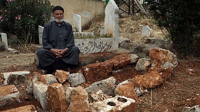 محمد حسن مسطو يجلس بجوار قبر شقيقه لطفي في 7 مايو 2023، في قرية قرقانيا، وهي منطقة ريفية شمال محافظة إدلب، سوريا