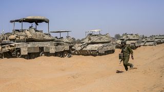 An Israeli soldier walks past a line of tanks at a staging ground near the border with Gaza in southern Israel, May 5, 2024