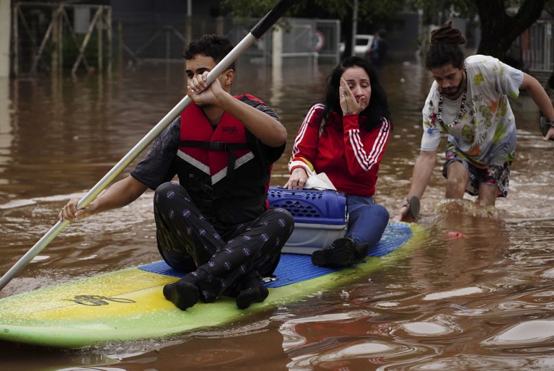 People evacuate on a surfboard from a neighborhood flooded by heavy rains, in Canoas, Rio Grande do Sul state, Brazil