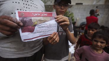 Palestinians hold leaflets dropped by Israeli planes calling on them to evacuate ahead of an Israeli military operation in Rafah, southern Gaza Strip, Monday, May 6, 2024. 