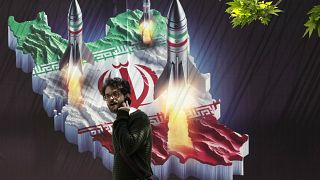 Un homme passe devant une bannière montrant des missiles lancés depuis une carte iranienne à Téhéran, le 19 avril 2024.