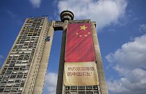 Des travailleurs s’accrochent à des cordes pour installer un drapeau national chinois sur un gratte-ciel menant à l’aéroport de Belgrade, en Serbie le samedi 4 mai 2024. 
