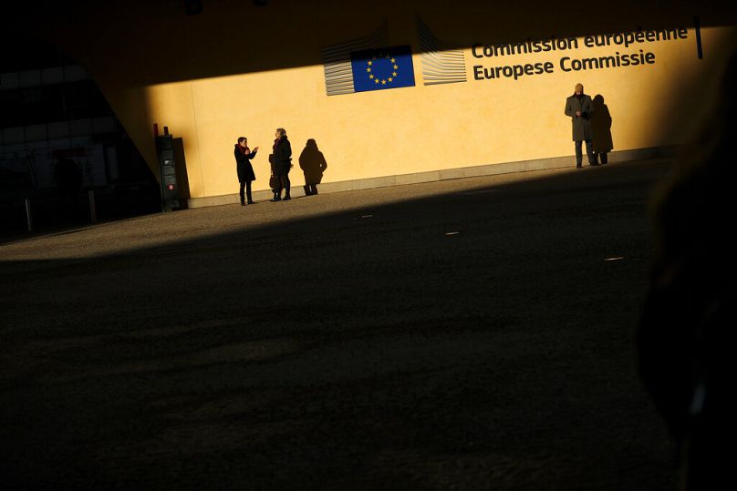 People stand under the sun at the entrance of the European Commission headquarters in Brussels, December 2019