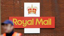 A British Royal Mail logo is seen behind a postal worker walking at a delivery office in London, Monday, Oct. 19, 2009. 