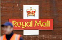 A British Royal Mail logo is seen behind a postal worker walking at a delivery office in London, Monday, Oct. 19, 2009.