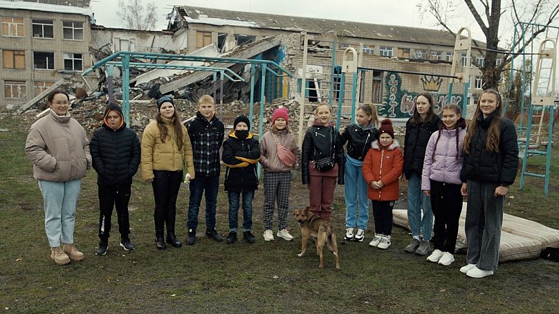 Schoolgirls stand outside the rubble of Velykokostromska School