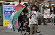 Un ciudadano lleva una bandera palestina y un cartel de protesta.
