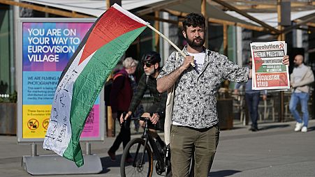 Un ciudadano lleva una bandera palestina y un cartel de protesta.