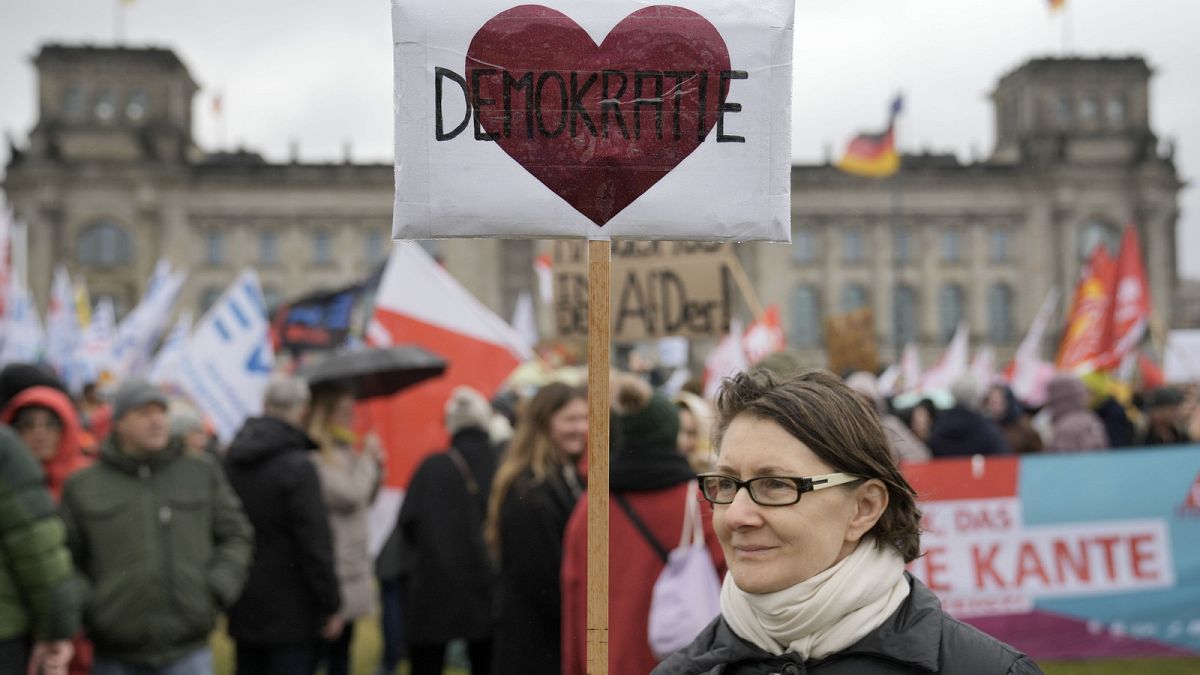 Un manifestante sostiene un cartel en el que se lee "Democracia" frente al Reichstag durante una manifestación contra el partido AfD y el extremismo de derechas en Berlín, febrero de 2024.
