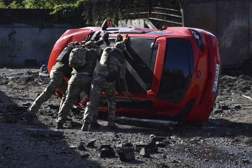Ukrainian servicemen turn over a damaged car at the scene of a Russian missile attack in Zaporizhzhia.