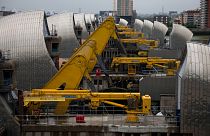 Yellow rocking beams stand raised as the rising sector gates of the Thames Barrier.
