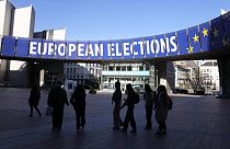 A group stands under an election banner outside the European Parliament in Brussels on April 29, 2024. 