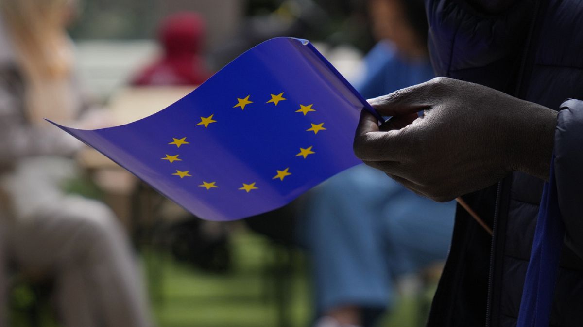 A man holds a European Union flag as he walks outside the European Commission building during Europe Day celebrations in Brussels on May 4, 2024.