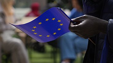 Un hombre sostiene una bandera de la Unión Europea mientras camina frente al edificio de la Comisión Europea durante las celebraciones del Día de Europa en Bruselas el 4 de mayo de 2024.
