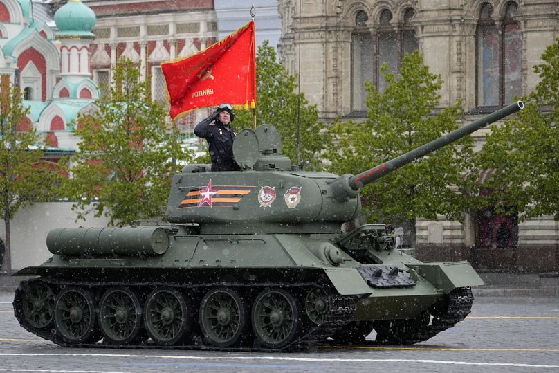 Üzerinde kırmızı bayrak bulunan Sovyet dönemine ait bir T-34 tankı Kızıl Meydan&apos;daki askeri geçit töreninde seyrederken