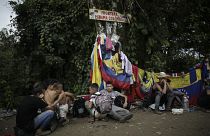 Migrantes sentados bajo una señal que marca la frontera entre Panamá y Colombia durante su travesía por el Tapón del Darién.