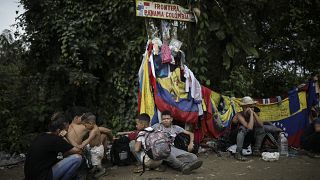 Migrantes sentados bajo una señal que marca la frontera entre Panamá y Colombia durante su travesía por el Tapón del Darién.