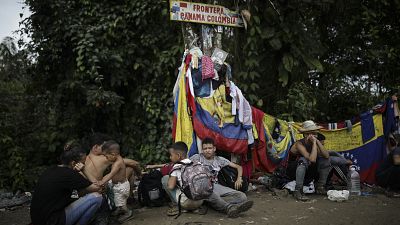 Migrants sit under a sign marking the Panama-Colombia border during their trek across the Darien Gap