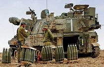 Gazze Şeridi dışında konuşlanan İsrail askerleri, bir topçu silahının yanında teçhizat hazırlarken 