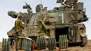 Gazze Şeridi dışında konuşlanan İsrail askerleri, bir topçu silahının yanında teçhizat hazırlarken 