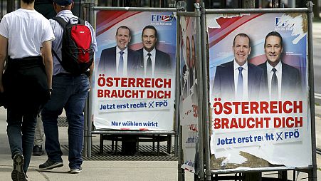 People pass by damaged election posters showing former Austrian Vice Chancellor and Interior Minister Heinz-Christian Strache, right in Vienna, Sunday, May 26, 2019. 