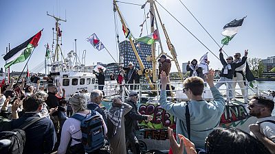 متظاهرون يرفعون الأعلام الفلسطينية على الرصيف باسم السفينة المتوجهة إلى غزة
