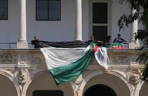 Estudantes e ativistas desenrolam uma bandeira palestiniana enquanto montam um acampamento no pátio da Universidade Estatal de Milão