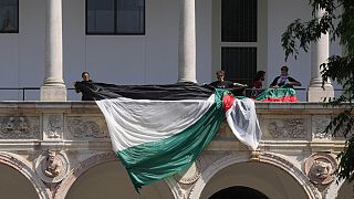Estudantes e ativistas desenrolam uma bandeira palestiniana enquanto montam um acampamento no pátio da Universidade Estatal de Milão