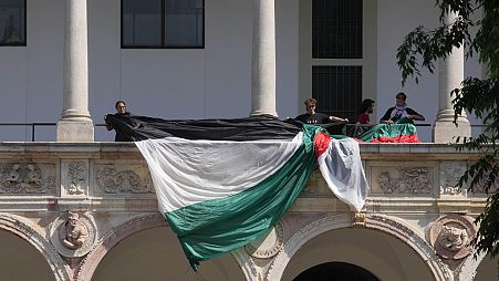 Estudantes e activistas desenrolam uma bandeira palestiniana enquanto montam um acampamento no pátio da Universidade Statale em Milão, Itália, sexta-feira, 10 de maio de 2024. 