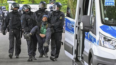 Német rendőrök cipelnek egy klímatüntetőt a Tesla raktáraként funkcionáló neuhardenbergi repülőtér közelében