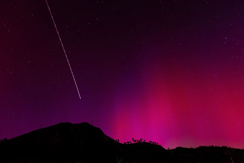 The blinking lights of a plane streak through the Aurora Borealis, also known as the Northern Lights, which is visible over Lake Berryessa, Calif., Saturday, May 11, 2024.