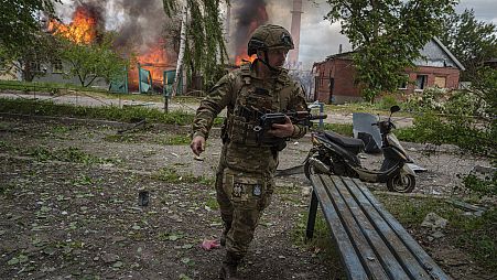 A police officer runs in front on burning house destroyed by a Russian airstrike in Vovchansk, Ukraine