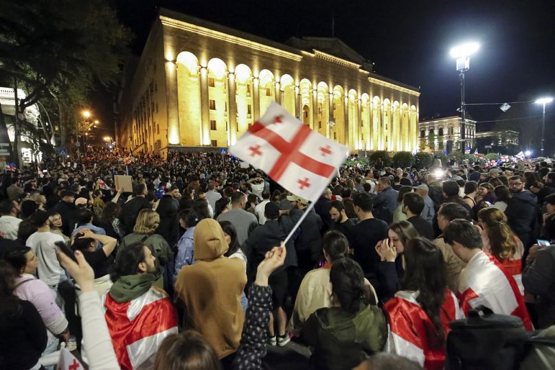 Manifestantes agitam uma bandeira nacional da Geórgia enquanto se concentram em frente ao edifício do parlamento em Tbilisi
