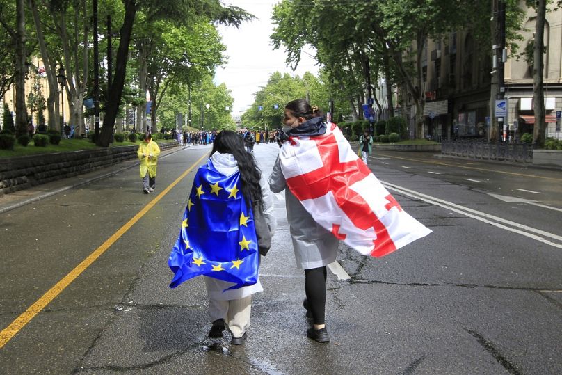 Two demonstrators with draped Georgian national and EU flags walk towards the Parliament building during a protest against "the Russian law" in Tbilisi. May 13, 2024