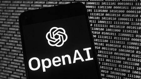 The OpenAI logo appears on a mobile phone in front of a computer screen with random binary data, Thursday, March 9, 2023, in Boston.