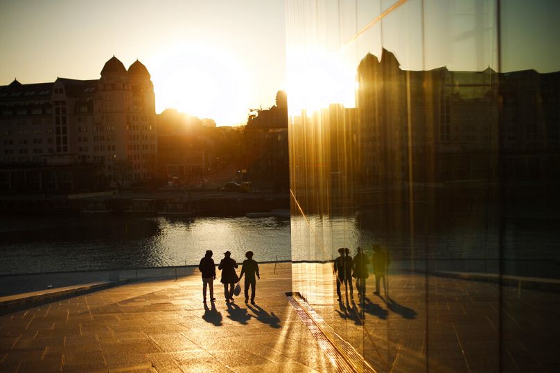 People walk at the Opera House as the sun sets in downtown Oslo, April 2021