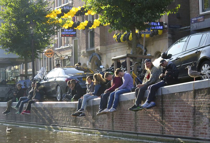 Tourists sit on the dock of a canal in front of a coffee shop in the centre of Amsterdam, October 2016
