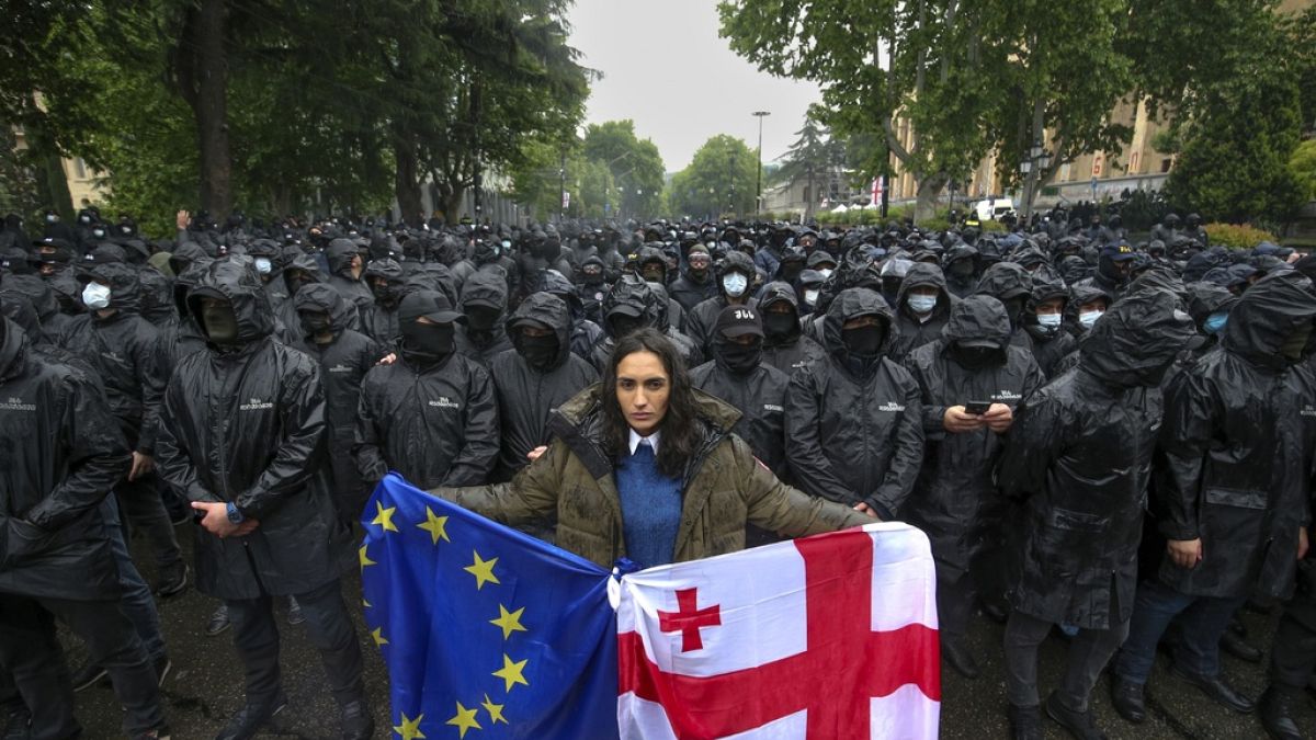 Una mujer sostiene una bandera de Georgia y otra de la UE frente a policías antidisturbios que bloquean una calle para impedir una protesta contra la 'ley rusa' en Tiflis.