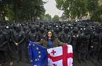 A woman holds a Georgian national and an EU flags in front of riot police