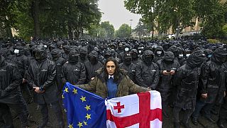 A woman holds a Georgian national and an EU flags in front of riot police blocking a street  (AP Photo/Zurab Tsertsvadze)