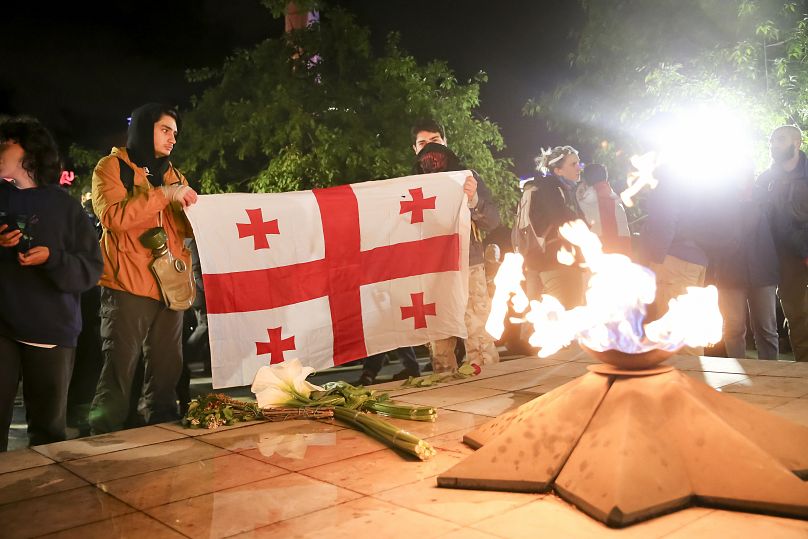 Demonstrators hold a Georgian national flag in front of an eternal flame at the Square of Heroes during an opposition protest in Tbilisi, May 14, 2024